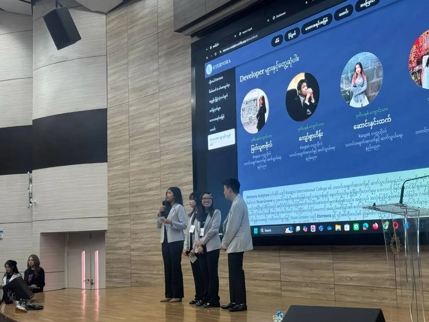 Team presenting on stage in front of a large screen showing the dashboard